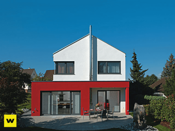 Modernes Einfamilienhaus mit roter Fassade und großem Garten bei blauem Himmel.