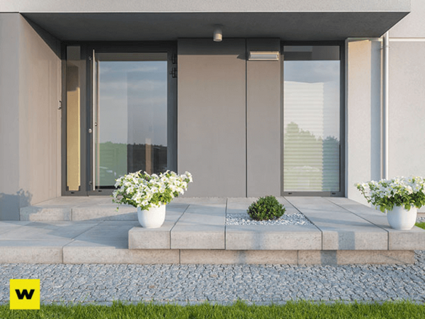 Moderner Hauseingang mit großen Glasflächen, Blumen in weißen Töpfen und Steinplatten.